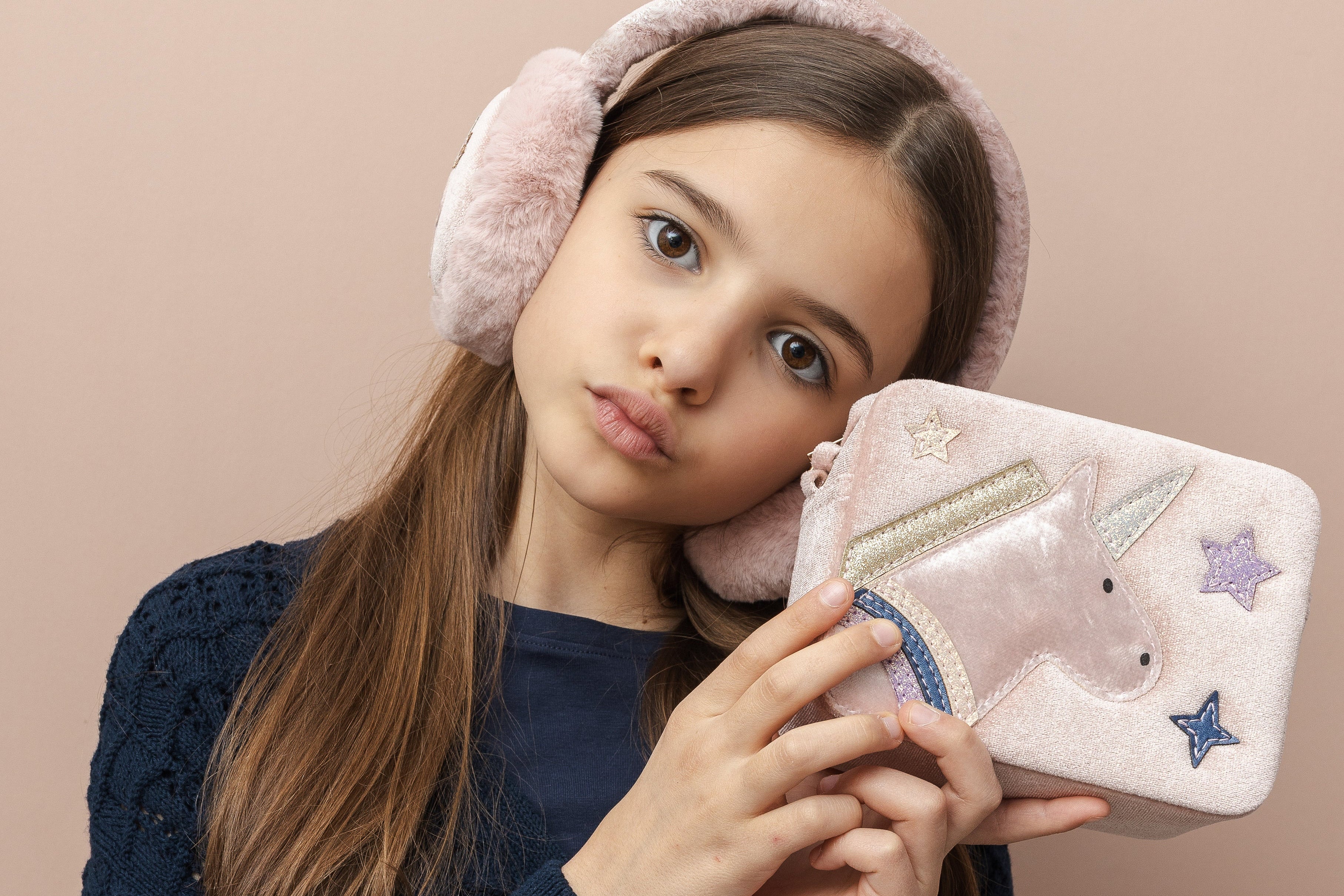 Young girl holding a unicorn-themed pouch against a beige background