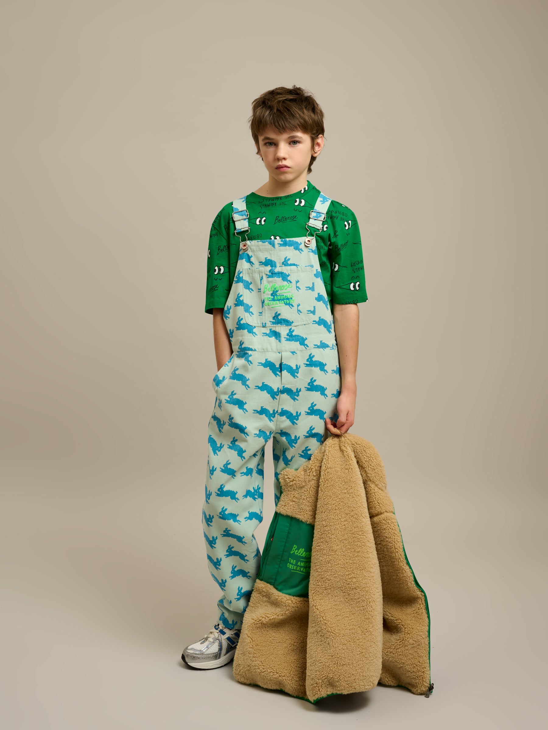 Boy wearing Bellerose X The Animals Observatory t shirt and overalls holding a jacket