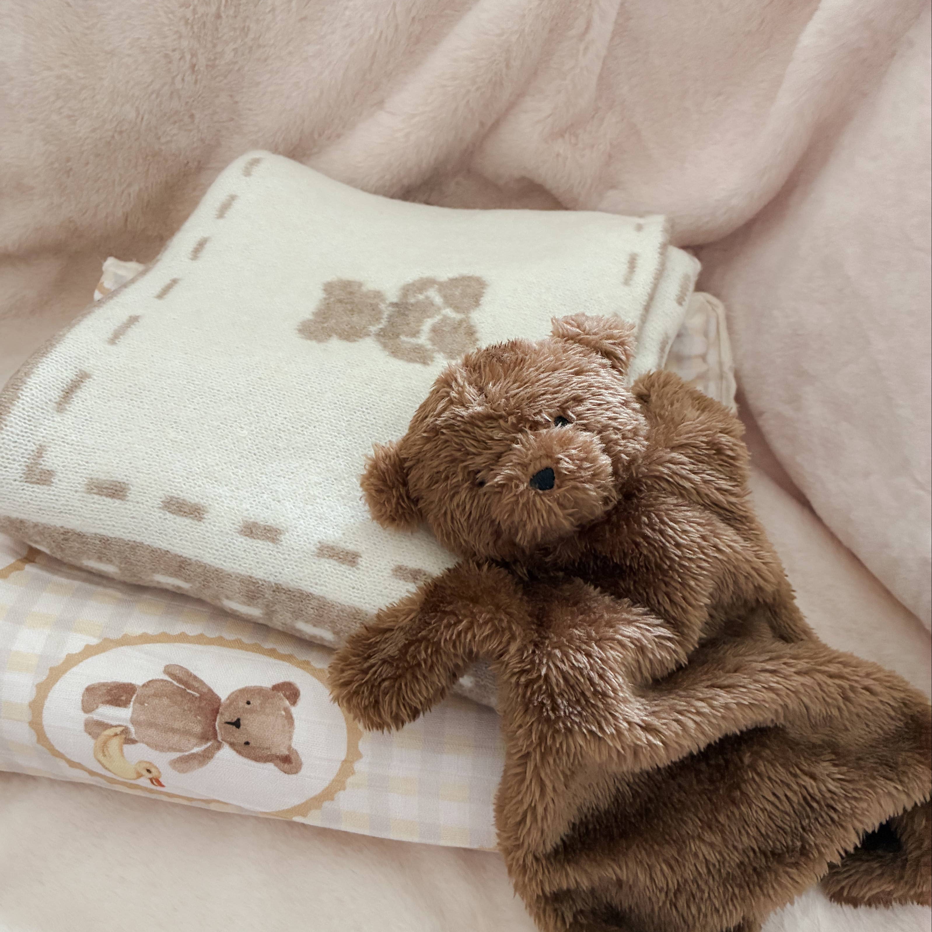 Brown teddy bear sitting on top of a folded baby blanket with teddy bear designs.