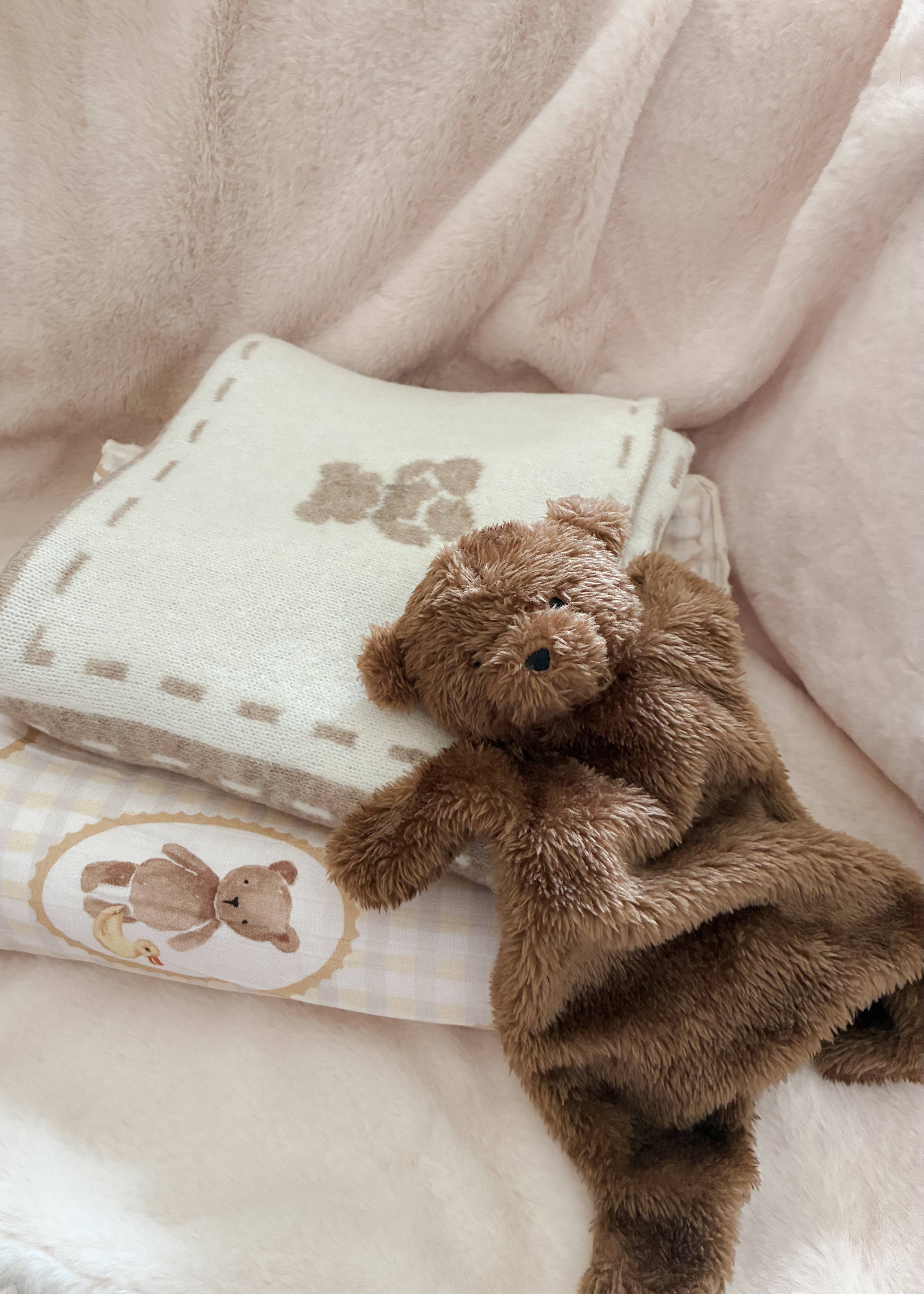 Brown teddy bear sitting on top of a folded baby blanket with teddy bear designs.